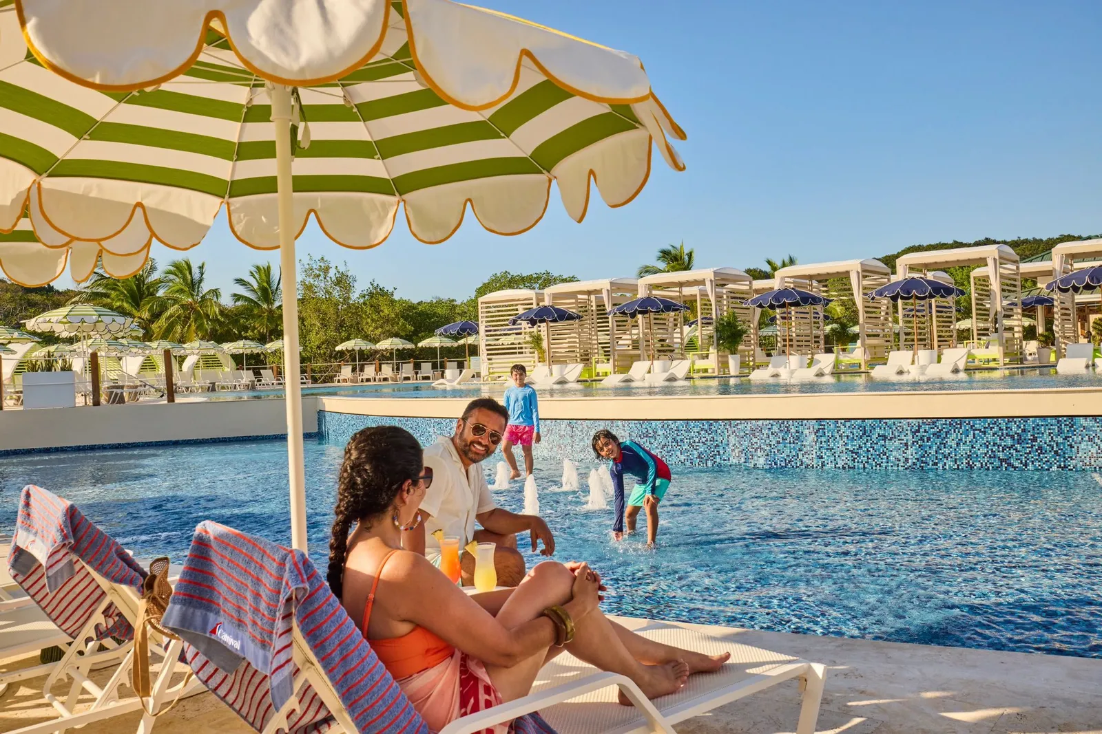 Guests relaxing on beach loungers under an umbrella at Isla Tropicale Roatan